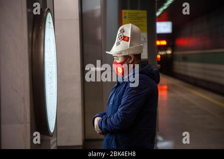 Moskau, Russland. Mai 2020. Ein Mann mit kirgisischem Kopfschmuck und Maske in den Farben der Flagge Kirgisistans schaut sich die Karte der Moskauer Metro an einer U-Bahnstation in Moskau während der Novel-Coronavirus COVID-19-Epidemie in Russland an Stockfoto