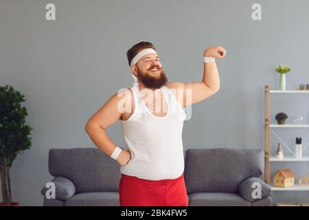 Lustiger fetter Mann in roten Shorts und weißem T-Shirt lächelnd Übungen im Raum machen Stockfoto