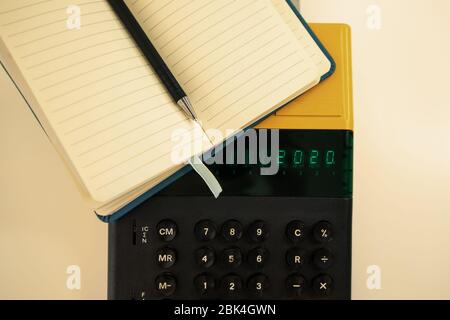 Altes Computermodell aus den 80er Jahren auf weißem Hintergrund, es ist eingeschaltet, es schreibt 2020 und ein Notizbuch mit einem Stift bereit für Notizen. Stockfoto