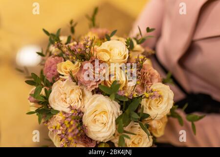 Goldene Trauringe auf einem Hochzeitsstrauß aus gelben und lila Rosen. Hochzeitstag. Nahaufnahme eines zugeschnittenen Rahmens. Strauß der Braut Stockfoto