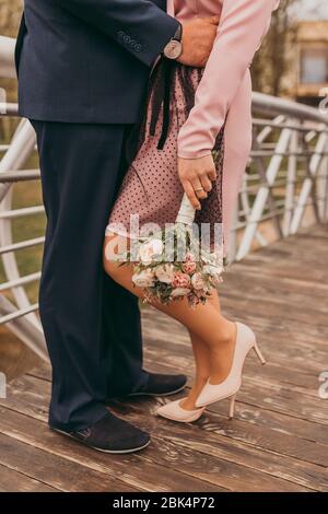 Nahaufnahme männliche und weibliche Beine, frisch vermählte stehend auf einer Holzbrücke und Braut mit einem Strauß. Hochzeitstag. Stockfoto