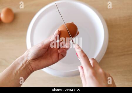 Frau bricht ein Ei mit einem Messer über einem Teller Um eine köstliche Mahlzeit zu kochen Stockfoto