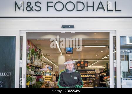 Reigate, Surrey, UK-Mai 1,2020 - ein Ladenbetreuerin mit Gesichtsschutz reguliert den Zugang zum M&S Supermarkt, um Überbelegung und COVID-19 Verbreitung zu verhindern Stockfoto