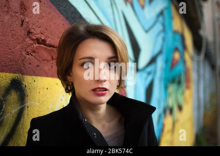 Weibliches Porträt des jungen Mädchens mit kurzen blonden Haaren in der Nähe der Wand mit Graffiti. Jugendkultur, Street-Art-Konzept Stockfoto