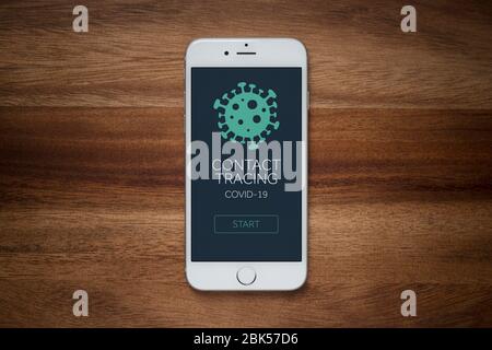 Ein Smartphone mit dem Startbildschirm einer fiktiven Covid-19-App zur Kontaktverfolgung liegt auf einem einfachen Holztisch (nur für redaktionelle Zwecke). Stockfoto