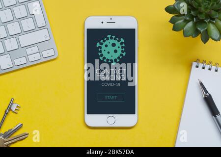 Ein iPhone mit einer fiktiven Covid-19-App zur Kontaktverfolgung auf einem gelben Tisch mit Tastatur, Tasten, Notizblock, Pflanze (nur Editorial). Stockfoto