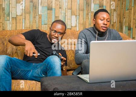 Zwei schöne afrikaner Jungs sitzen auf der Couch spielen Videospiele mit Joystick, Spiel Pad, Pad Stockfoto