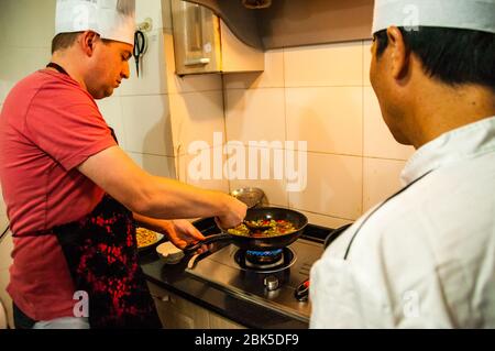 Koch Ding beauftragt ein ausländischer Tourist in wie Rindfleisch kochen mit Paprika in einem Koch in Shanghai Klasse. Stockfoto