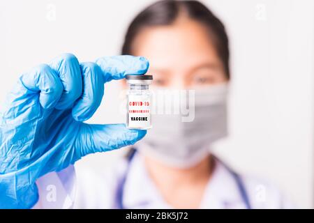 Asiatische Frau Arzt oder Krankenschwester in Uniform und Handschuhe tragen Gesichtsmaske Schutz im Labor hält Fläschchen Corona Impfstoff Flasche auf der Hand und bot Stockfoto
