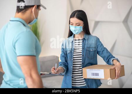 Frau mit einem Paket, das ein von einem Mann gehaltenes Dokument unterzeichnet. Stockfoto