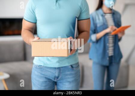 Mann in hellblauem T-Shirt mit Box, Frau mit Tablet. Stockfoto