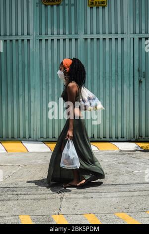 Junge Frau, die während der Sperrung des Coronavirus in Kolumbien Lebensmitteltaschen in der leeren Stadt trägt Stockfoto