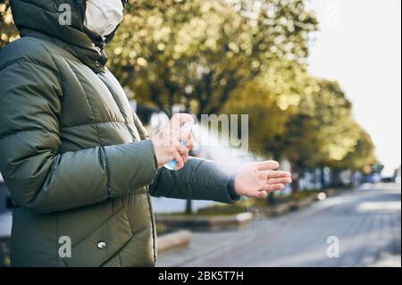 Ausschnitt-Schnappschuss von Händen einer Frau in Maske, auf der Straße, die ihre Hände mit Handwaschspray als vorbeugende Hygienemaßnahme gegen Covid-19-Infektion abwischt. Soziale Distanz bewahren Stockfoto