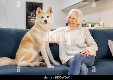 Ruhestand. Ältere Frau zu Hause sitzend streichelte akita inu lächelnd fröhlich Stockfoto