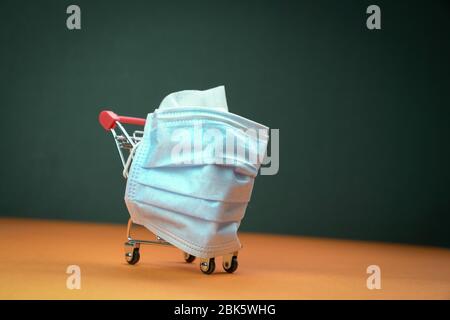 Einkaufswagen oder Trolley mit medizinischer Gesichtsmaske umwickelt. Isoliert. Konzeptionell. Stockfoto