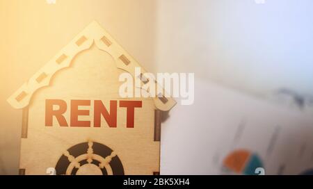 Miniatur-Spielzeug-Modellhaus mit Inschrift MIETEN Buchstaben Wort auf Holzhintergrund. Immobilien-Versicherung süße Haus mieten Konzept Stockfoto