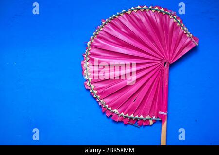 Palm Leaf Handventilatoren isoliert mit blauem Hintergrund. Handgefertigte rosa Palmblatt Handventilatoren zum Verkauf in der Sommersaison. Stockfoto