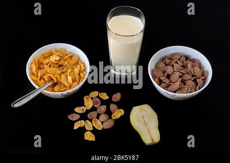 Mais Choco Flocken Getreide in Schüssel mit Milch und Birne Scheiben auf schwarz grauen Hintergrund isoliert, ein leckeres und gesundes diätetisches Frühstück. Draufsicht Stockfoto