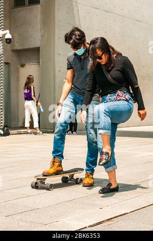 Eine junge Chinesin lehrt einen ausländischen Mann vor dem Long Museum West Bund, Shanghai, China, Skateboard fahren. Stockfoto