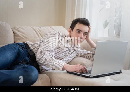 Junger Mann, der auf sofat liegt und zu Hause einen Laptop benutzt Stockfoto