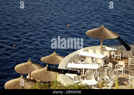 Griechenland, Insel Hydra, Tische und Stühle des Restaurants neben alten Kanonen im Hafen der Insel. Stockfoto