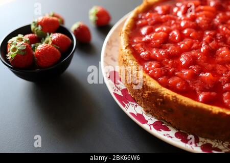 Bäckereikonzept. Hausgemachter Käsekuchen mit Erdbeersoße auf dem Tisch. Frische Erdbeeren auf Hintergrund. Draufsicht Stockfoto