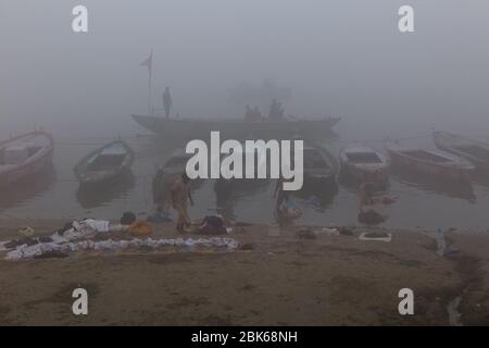 Eine neblige morgendliche Bootsfahrt und Menschen waschen Kleidung in kühlen Morgen am Ufer des Flusses Ganges, Varanasi, Indien Stockfoto