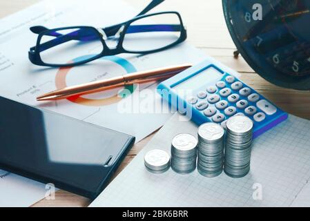 Draufsicht Münzen Stapel und Rechner und smartphne und Gold Stift und Gläser schmücken auf Arbeitstisch. Stockfoto