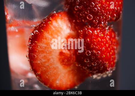 Makro-Nahaufnahme aus isoliertem Cocktailglas mit roten Erdbeeren, spritzigen Tonic Water und Eiswürfeln Stockfoto
