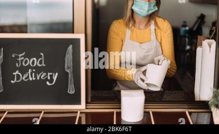 Junge Frau bereitet Lieferkost im Restaurant zum Mitnehmen während der Coronavirus-Ausbruch-Periode - Arbeiter in der Küche Kochen gesunde Lebensmittel für hom Stockfoto