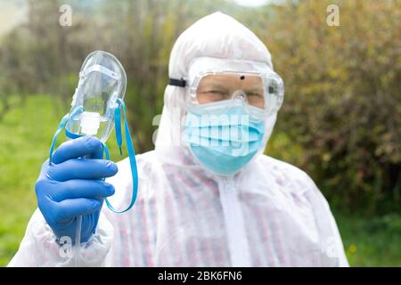 Portrait des älteren Mannes trägt Hasmatanzug, Brille, Maske und Handschuhe hält eine Sauerstoffmaske im Freien Stockfoto