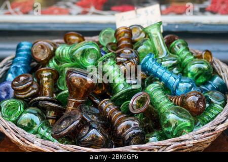 Kleine grüne, braune und blaue Glasflaschen oder Schmuckstücke zum Verkauf in einem runden Korb vor dem Geschäft Stockfoto