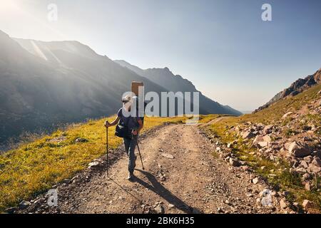Wanderer mit grossen Rucksack zu Fuß auf der Straße mit spektakulären Bergen im Hintergrund Stockfoto