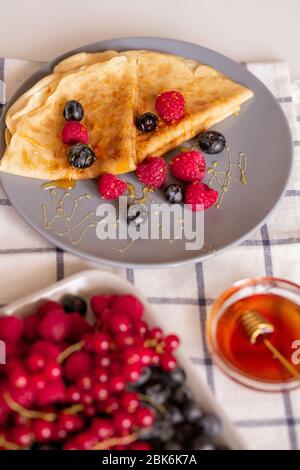 Teller mit zwei gefalteten appetitlichen Pfannkuchen mit Honig und frischen Himbeeren und Brombeeren auf Küchentisch zum Frühstück serviert Stockfoto