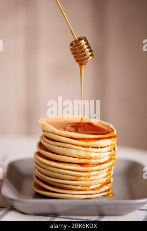 Frischer, leckerer Honig wird während des Kochens auf den appetitlichen hausgemachten Pfannkuchen auf den Teller gegossen Stockfoto