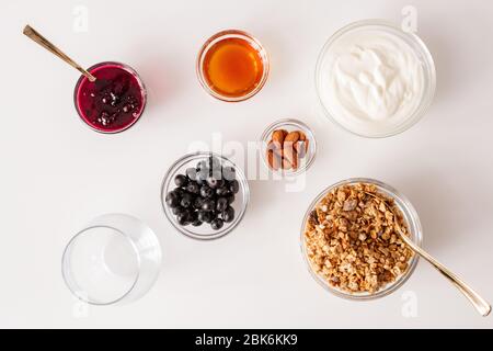 Flacher Grundriss mit weißem Küchentisch mit mehreren Schalen mit Müsli, Kirschmarmelade, Sauerrahm, Mandelkernen, Honig und frischen Brombeeren Stockfoto