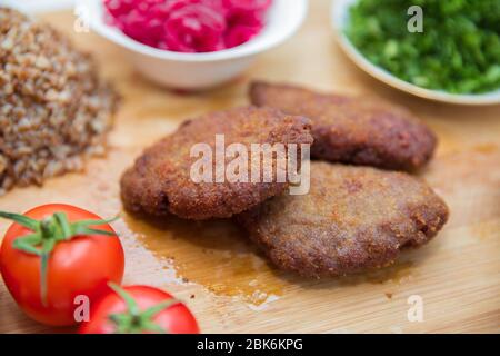 Fleischschnitzel, gebackener Buchweizen auf einem Holzbrett. Rotkohl-Sauerkraut . Knoblauch, Zwiebeln, Tomaten. Gehackter Koriander. Hausgemachte Koteletts mit Haferflocken Stockfoto