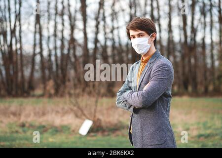 Gutaussehender junger Mann, der im Freien steht und eine medizinische Maske trägt, um andere vor der Verbreitung von Viren zu schützen Stockfoto