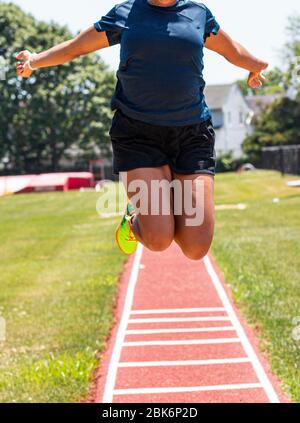 Eine High School weibliche Leichtathletin übt die Weitsprung-Anzeige fliegen in der Luft an der Kamera. Stockfoto