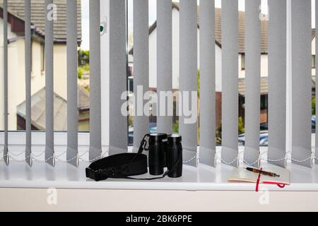 Notebook und Fernglas für den Blick durch ein Fenster, um zu spionieren und zu berichten, dass Nachbarn während des neuen Covid-19-Ausbruchs die Sperrregeln brechen. Großbritannien Stockfoto