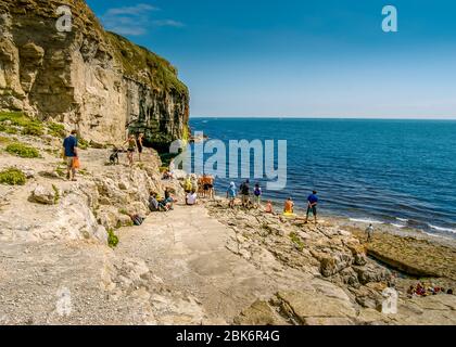 Touristen blicken an einem sonnigen Sommernachmittag vom felsigen Dancing Ledge, Langton Matravers, nahe Swanage, Dorset, Großbritannien, auf das Meer Stockfoto