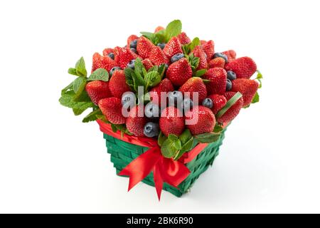 Weidenkorb mit saftigen Erdbeeren, Heidelbeeren mit frischen Minzblättern auf weißem Hintergrund verziert. Stockfoto