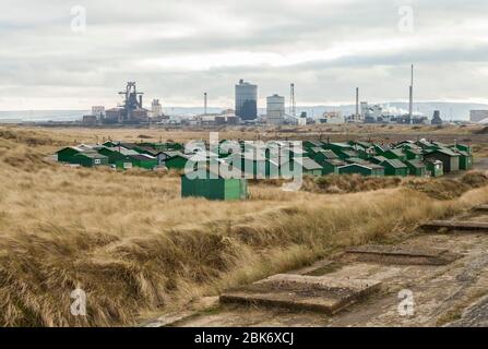 Die fishermens Hütten am South Gare, Redcar, England, UK mit der ehemaligen SSI Stahlwerk im Hintergrund Stockfoto