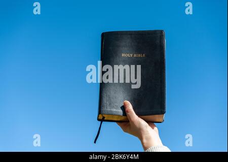 Erhobene Hand, die die Heilige Bibel hält. Hintergrund mit blauem Himmel an einem schönen Wintermorgen. Kopierbereich. Nahaufnahme. Horizontale Aufnahme. Stockfoto
