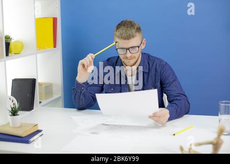 Konzentrierter Designer, der auf Bleistift schaut, skizziert Layout, der Bleistift am Tempel hält Stockfoto