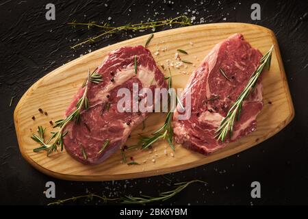 Ein Paar saftige rohe Fleischstücke mit Gewürzen liegen auf einem Holzbrett. Stockfoto