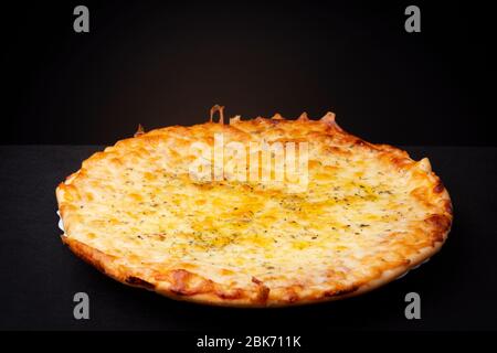 Vier Käse hausgemachte Pizza ohne Belag und mit knusprigen Wappen und goldgelb orange Tönung Studio Low-Key Stillleben vor einem dunklen Hintergrund Stockfoto