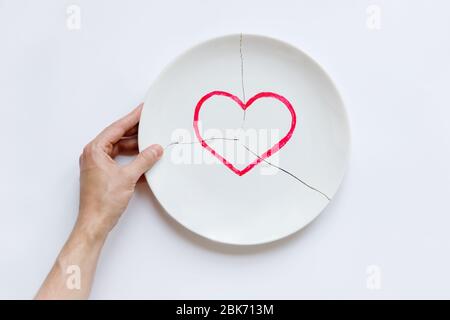 Draufsicht der Menschenhand, die eine gebrochene weiße Platte mit Herz-Symbol hält. Metapher für Scheidung, Beziehungen, Freundschaften, Riss in der Ehe. Die Liebe ist weg Stockfoto