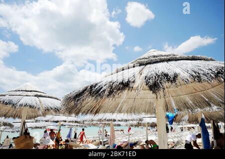 Menschen genießen zusammen im bunten türkisfarbenen Meerwasser an sonnigen Tag in schönen Strand. Strohschirme und viele Sonnenliegen an einem tropischen Strand nea Stockfoto