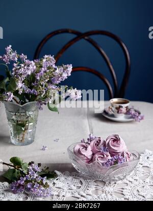 Atmosphärisch violett süß hausgemachte Zephyr oder Marshmallow aus schwarzen Johannisbeeren in der Nähe lila Blüten und Tasse Kaffee auf grauen Tischtuch und dunklen backgroun Stockfoto